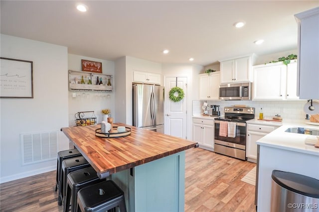 kitchen with backsplash, visible vents, appliances with stainless steel finishes, light wood-type flooring, and butcher block countertops