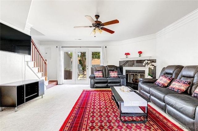 carpeted living area featuring stairs, a ceiling fan, a glass covered fireplace, and ornamental molding
