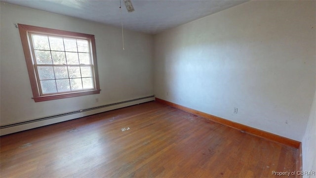 spare room featuring baseboards, a baseboard heating unit, and wood finished floors