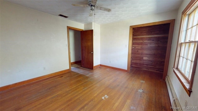 spare room featuring ceiling fan, baseboards, wood finished floors, a baseboard radiator, and visible vents