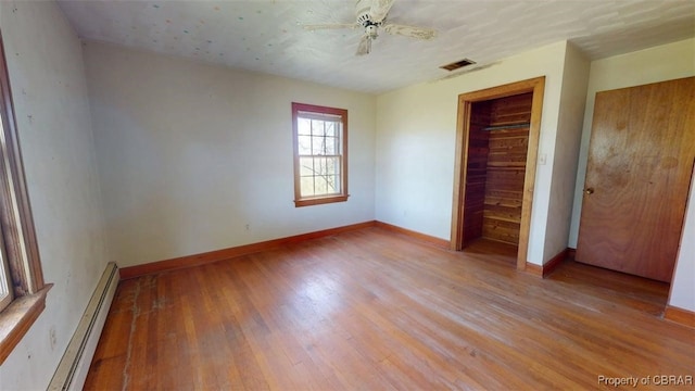 unfurnished bedroom with visible vents, baseboards, a closet, a baseboard heating unit, and light wood-style flooring