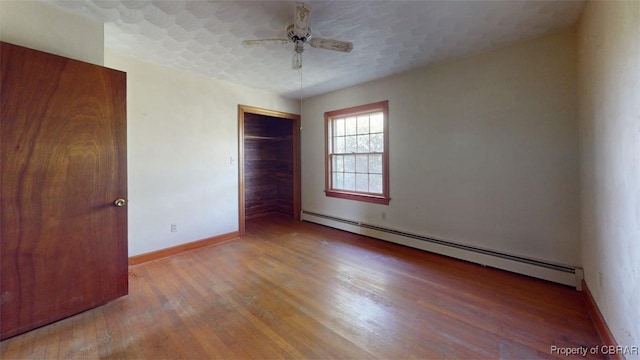spare room with baseboards, ceiling fan, a baseboard heating unit, and wood finished floors