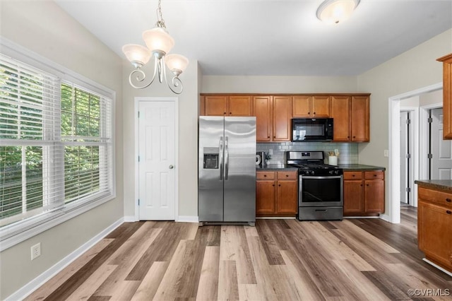 kitchen with stainless steel appliances, dark countertops, brown cabinetry, light wood-style flooring, and a chandelier