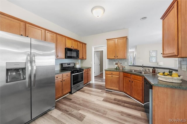kitchen featuring appliances with stainless steel finishes, a sink, dark countertops, and light wood finished floors