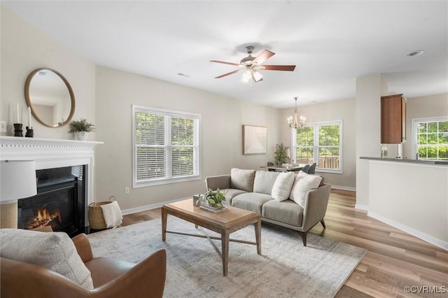 living room with a chandelier, a glass covered fireplace, baseboards, and light wood-style floors