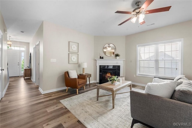 living area featuring a glass covered fireplace, wood finished floors, a ceiling fan, and baseboards