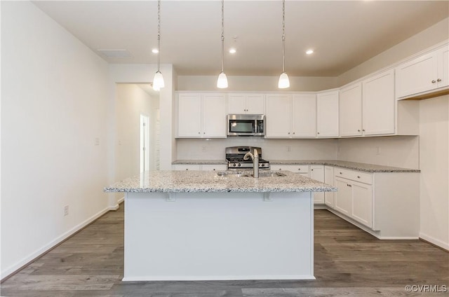 kitchen with appliances with stainless steel finishes, wood finished floors, a sink, light stone counters, and white cabinets