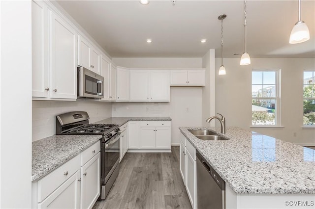 kitchen with white cabinets, appliances with stainless steel finishes, a sink, a kitchen island with sink, and light wood-style flooring