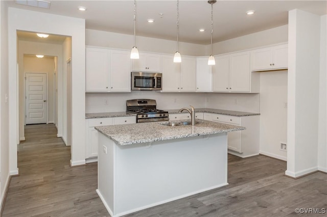 kitchen featuring white cabinets, light stone countertops, appliances with stainless steel finishes, a sink, and wood finished floors