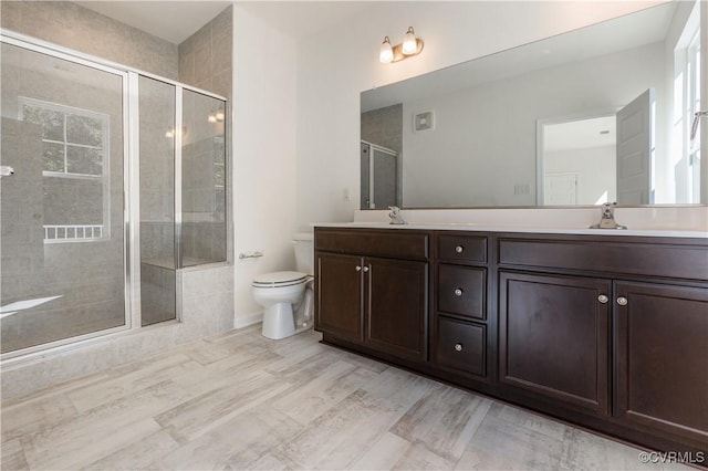 bathroom featuring double vanity, a stall shower, wood finished floors, a sink, and toilet
