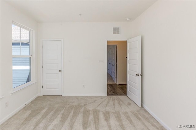 empty room with light colored carpet, baseboards, and visible vents