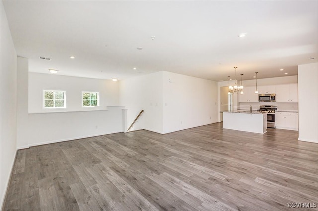 unfurnished living room featuring visible vents, recessed lighting, wood finished floors, and a chandelier