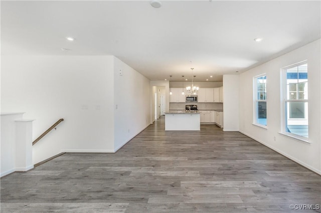 unfurnished living room featuring an inviting chandelier, baseboards, recessed lighting, and wood finished floors