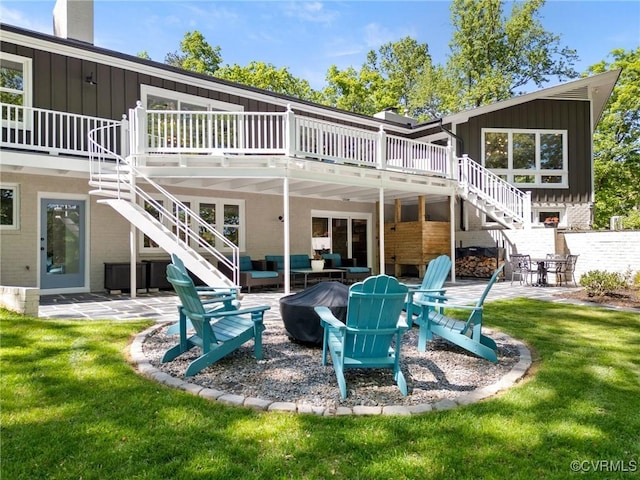rear view of house with an outdoor living space with a fire pit, a wooden deck, stairs, board and batten siding, and a patio area