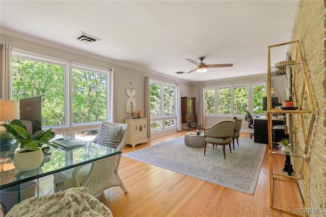 interior space with visible vents, a ceiling fan, ornamental molding, and light wood-type flooring