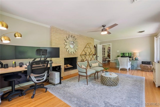 office featuring crown molding, ceiling fan, a fireplace, wood finished floors, and visible vents