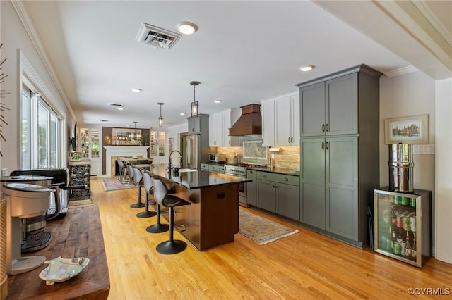 kitchen with dark countertops, a sink, premium range hood, premium appliances, and visible vents