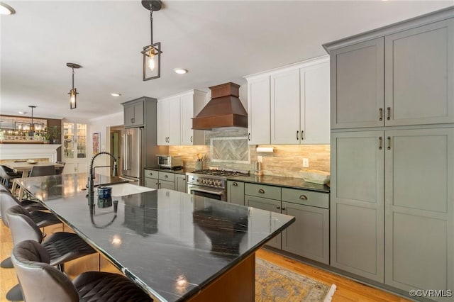 kitchen with a kitchen breakfast bar, premium range hood, decorative backsplash, light wood-type flooring, and premium appliances