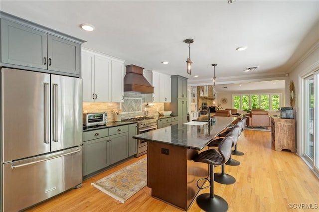 kitchen featuring backsplash, high quality appliances, a center island with sink, premium range hood, and open floor plan