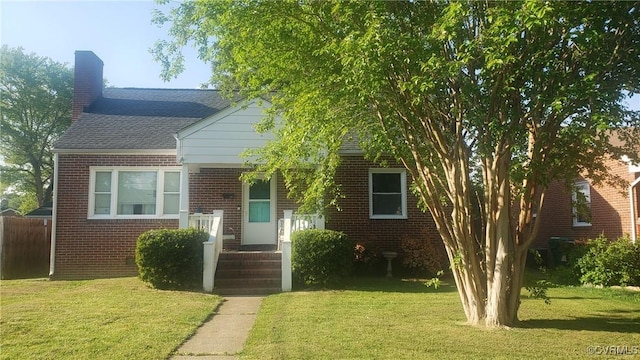 bungalow with roof with shingles, fence, brick siding, a front yard, and a chimney
