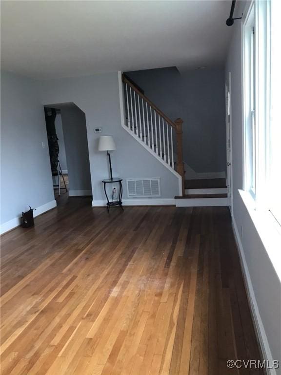 unfurnished living room featuring baseboards, visible vents, wood finished floors, and stairway