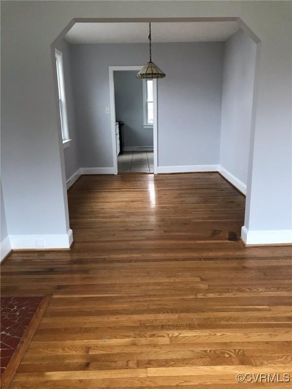 unfurnished dining area featuring arched walkways, baseboards, and wood finished floors