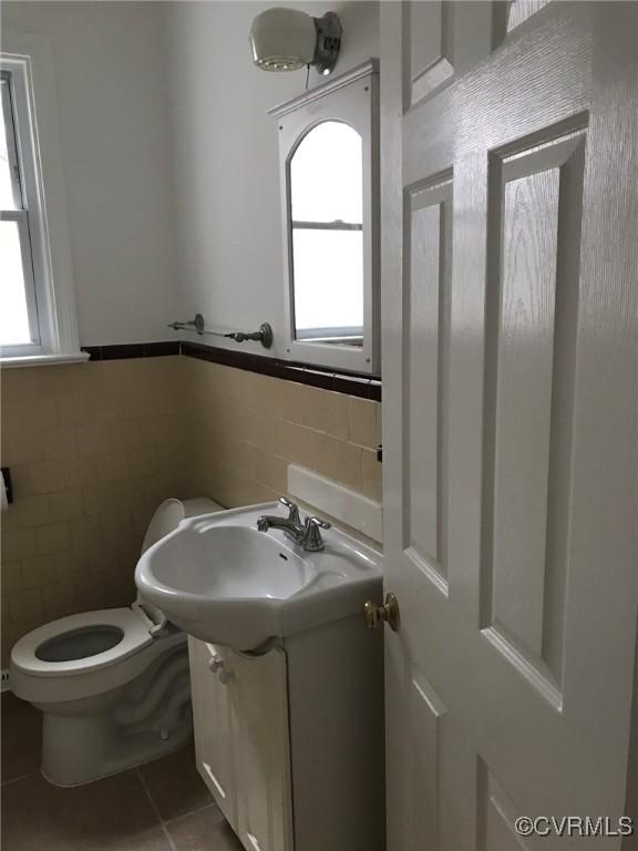 half bathroom with tile walls, tile patterned flooring, vanity, and a wealth of natural light