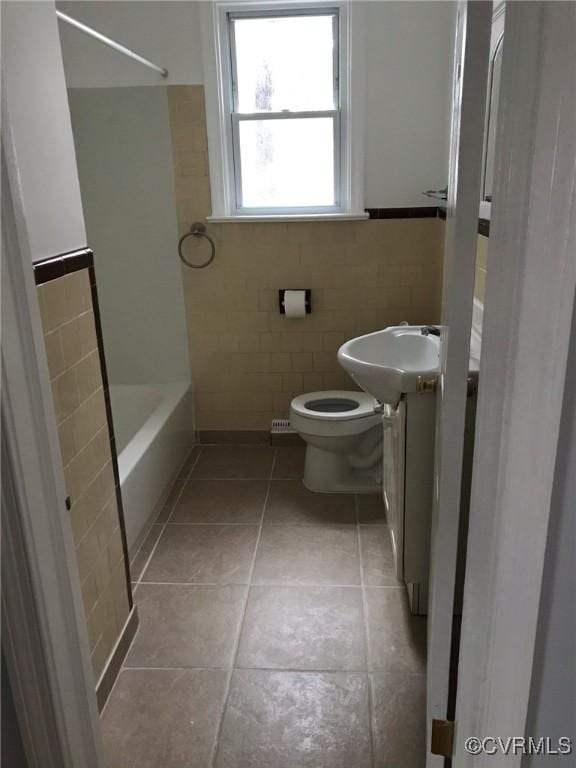bathroom featuring toilet, tile walls, shower / bathing tub combination, a wainscoted wall, and tile patterned floors