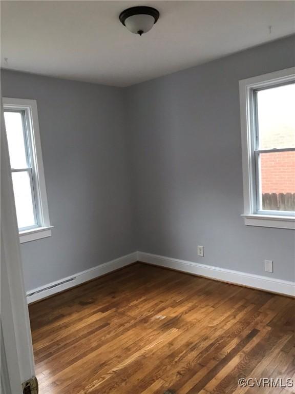 unfurnished room featuring baseboards, dark wood-type flooring, and a baseboard heating unit