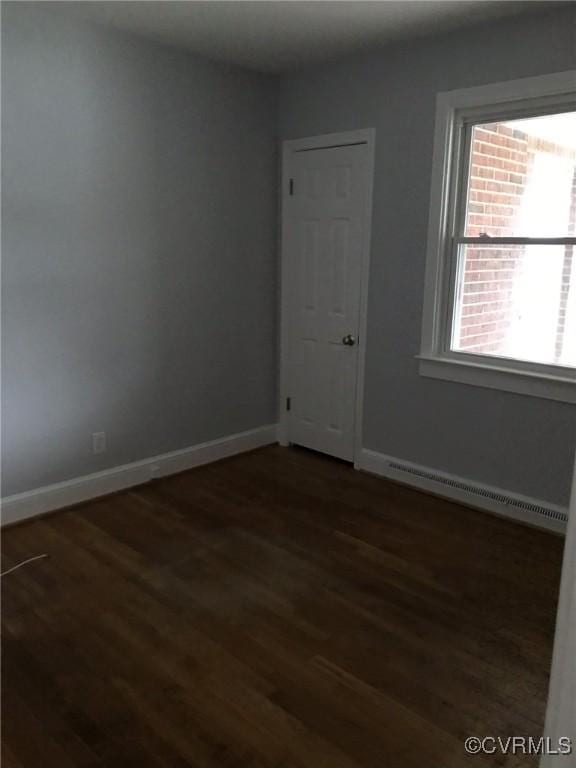 empty room with baseboards, a baseboard radiator, and wood finished floors