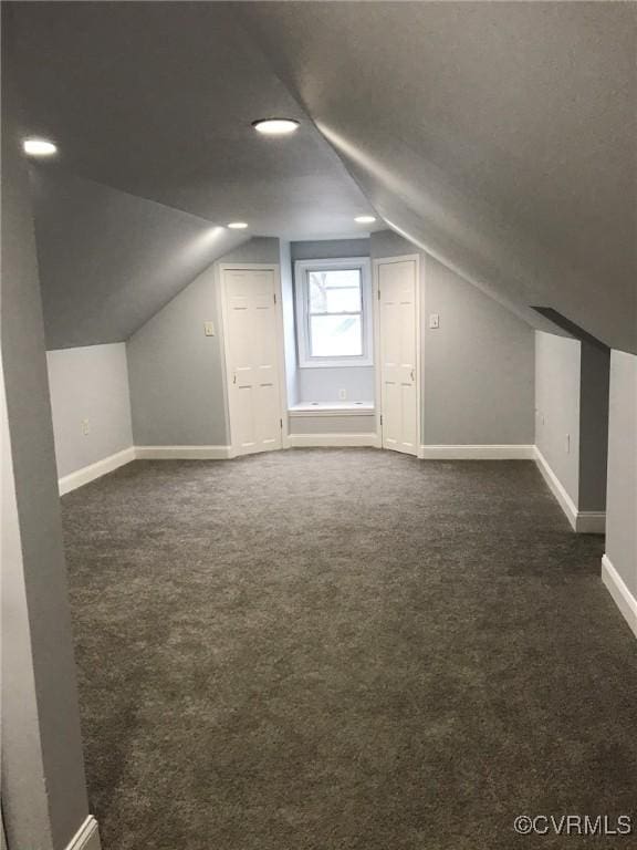 bonus room with baseboards, vaulted ceiling, and dark colored carpet
