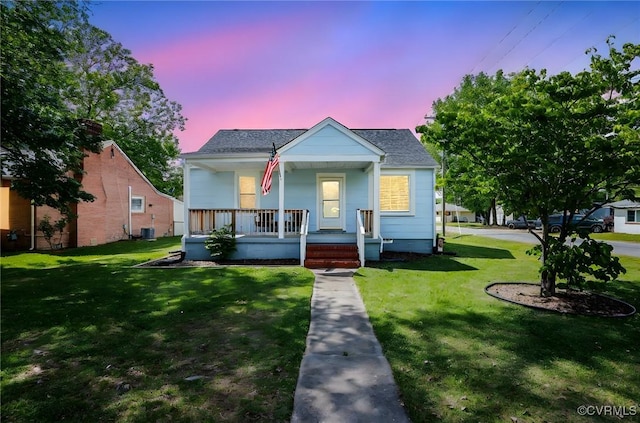 bungalow featuring a lawn, roof with shingles, central AC, and covered porch