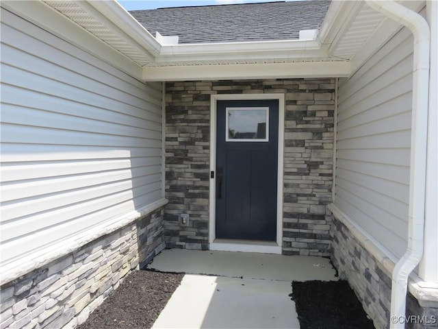 entrance to property featuring roof with shingles and stone siding