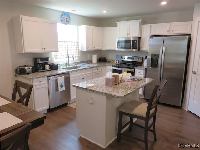 kitchen with a kitchen island, a breakfast bar, white cabinetry, a sink, and appliances with stainless steel finishes