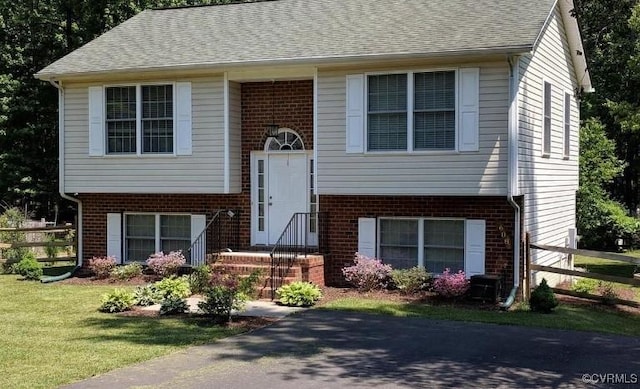 bi-level home with brick siding, fence, a shingled roof, and a front lawn