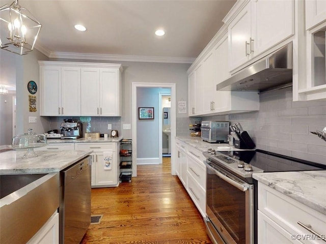 kitchen featuring a chandelier, stainless steel appliances, decorative backsplash, under cabinet range hood, and ornamental molding