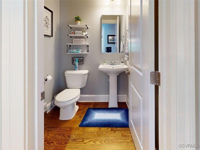 half bathroom with baseboards, toilet, and wood finished floors