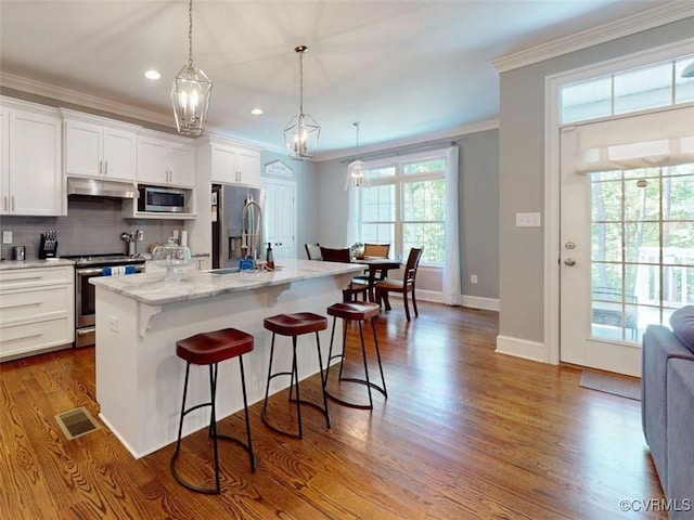 kitchen featuring appliances with stainless steel finishes, white cabinets, ornamental molding, a breakfast bar, and under cabinet range hood
