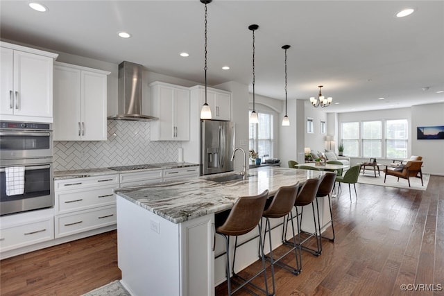 kitchen with appliances with stainless steel finishes, a sink, a breakfast bar area, wall chimney exhaust hood, and decorative backsplash