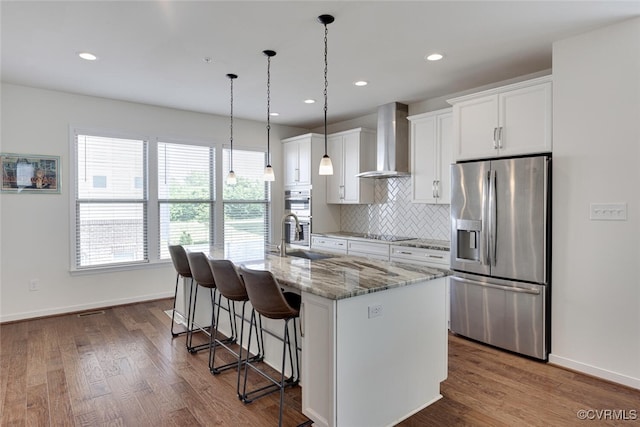kitchen with an island with sink, a kitchen breakfast bar, wall chimney range hood, white cabinets, and stainless steel appliances