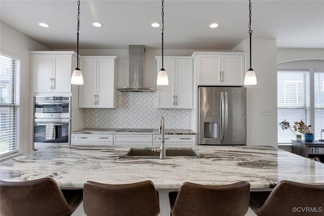 kitchen featuring wall chimney range hood, plenty of natural light, backsplash, a sink, and stainless steel appliances