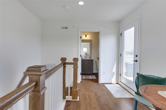 hallway with visible vents, wood finished floors, baseboards, recessed lighting, and an upstairs landing