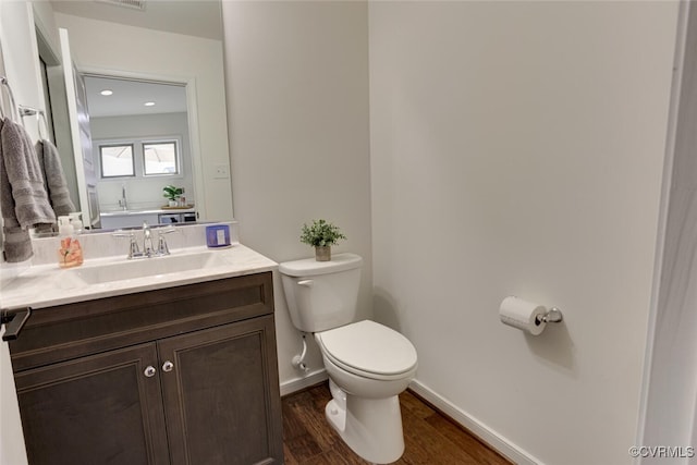 half bath featuring vanity, toilet, baseboards, wood finished floors, and visible vents