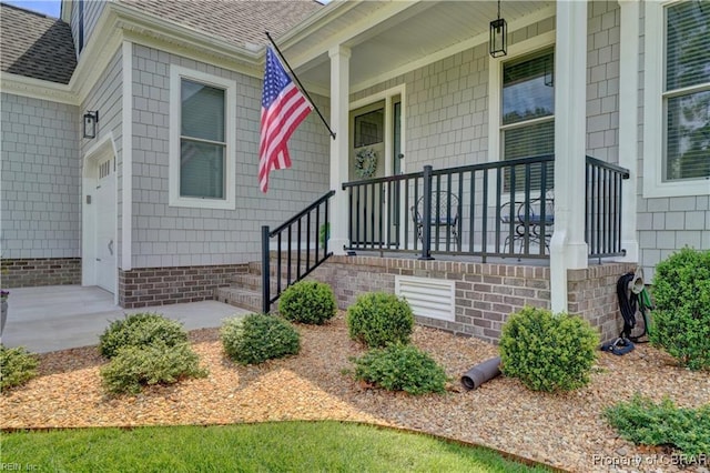view of exterior entry with a shingled roof and covered porch