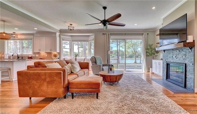 living room featuring ceiling fan, a stone fireplace, light wood finished floors, ornamental molding, and recessed lighting