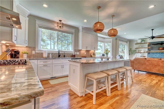 kitchen featuring decorative backsplash, a center island, stainless steel gas cooktop, under cabinet range hood, and white cabinetry