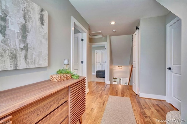 corridor featuring a barn door, baseboards, light wood finished floors, an upstairs landing, and recessed lighting