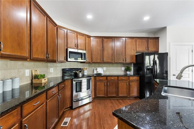 kitchen with appliances with stainless steel finishes, a sink, dark wood finished floors, backsplash, and visible vents