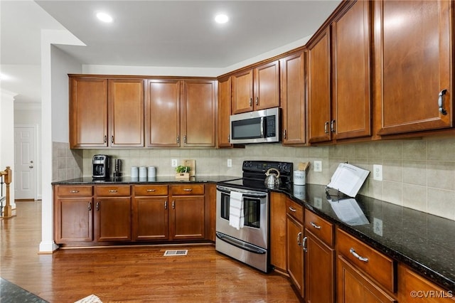 kitchen with appliances with stainless steel finishes, decorative backsplash, dark wood finished floors, and visible vents