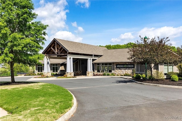 view of front facade featuring a shingled roof, a front yard, and stone siding